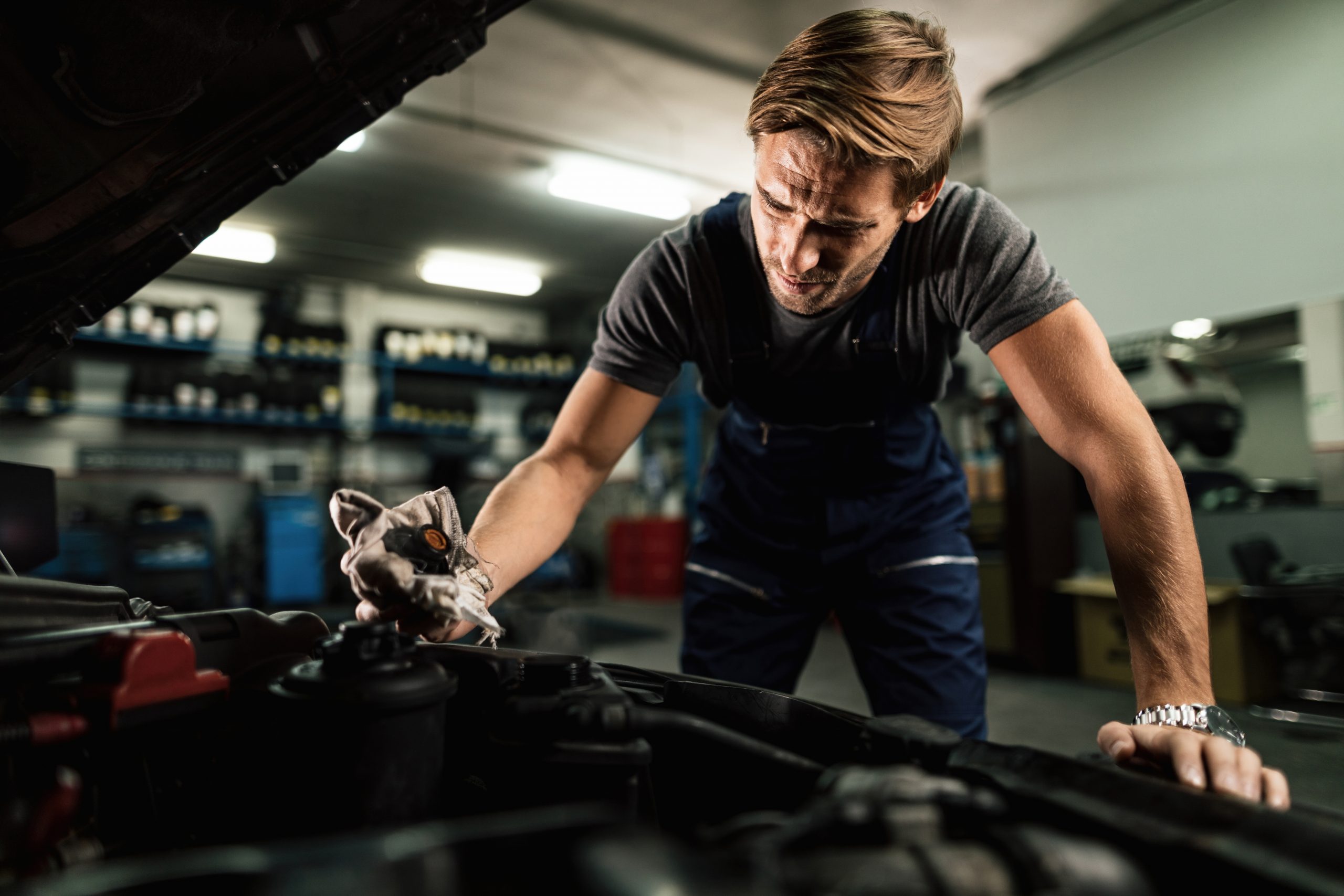 young mechanic checking car radiator system in auto repair shop.