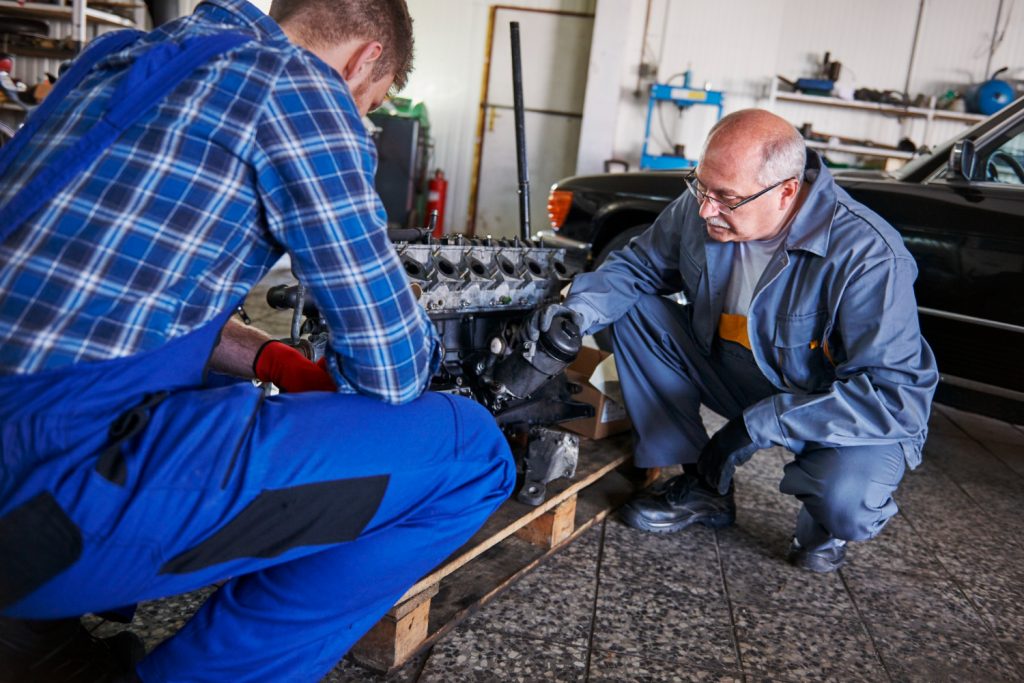 Two qualified technicians at PPC GARAGE performing mechanical repair on a car engine in the workshop.