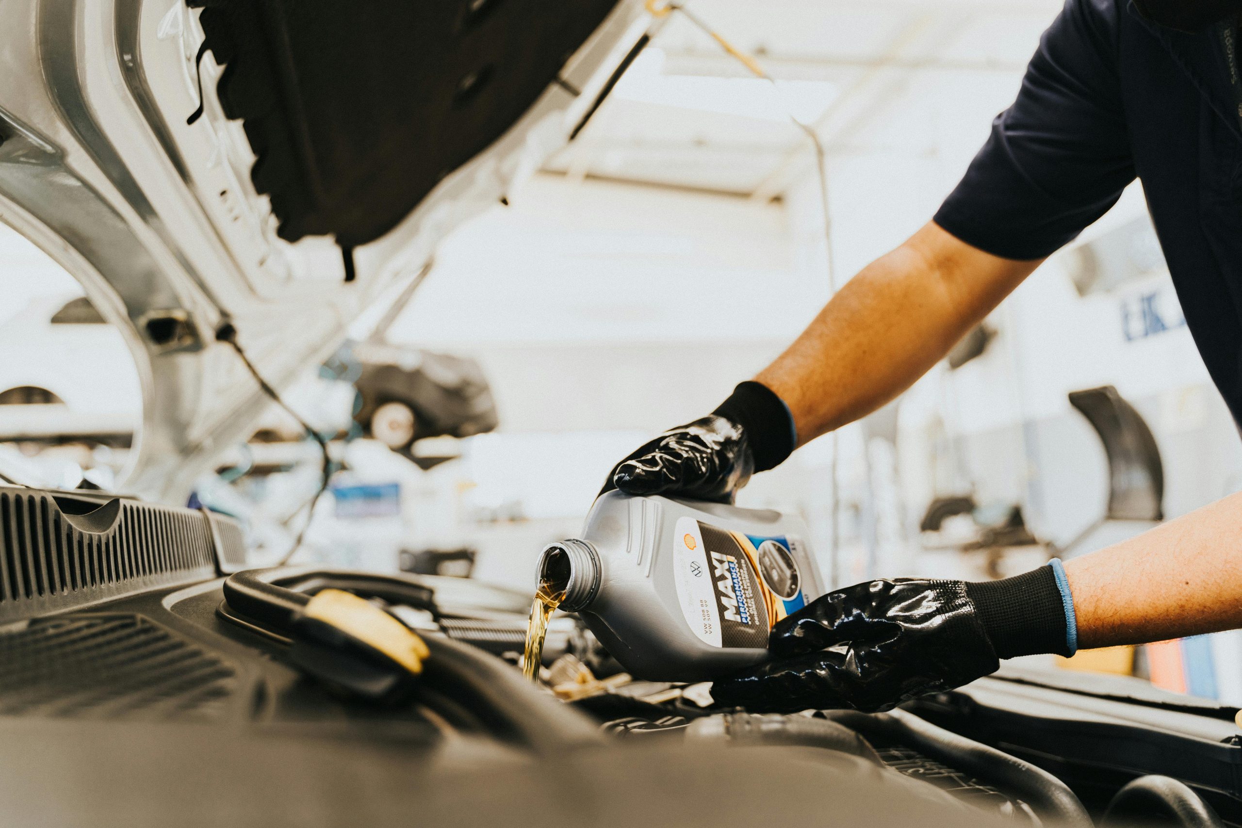 Close-up of a mechanic in PPC local garage in Birchington pouring engine oil in a car inside a garage. Hands wearing gloves.